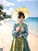 A woman in a blue and green kimono holding an umbrella on the beach.