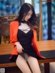 A woman in a black dress and orange jacket sitting on a table.