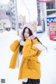 A woman in a yellow coat is standing in the snow.