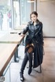 A woman in a black leather trench coat sitting at a table.