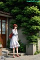 A woman in a white dress and red hat standing in front of a house.