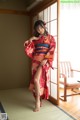 A woman in a red kimono standing in front of a window.