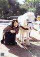 A woman kneeling down next to a small white horse.