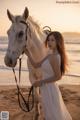 A woman in a white dress standing next to a white horse.