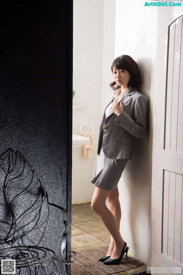 A woman in a gray suit leaning against a wall.