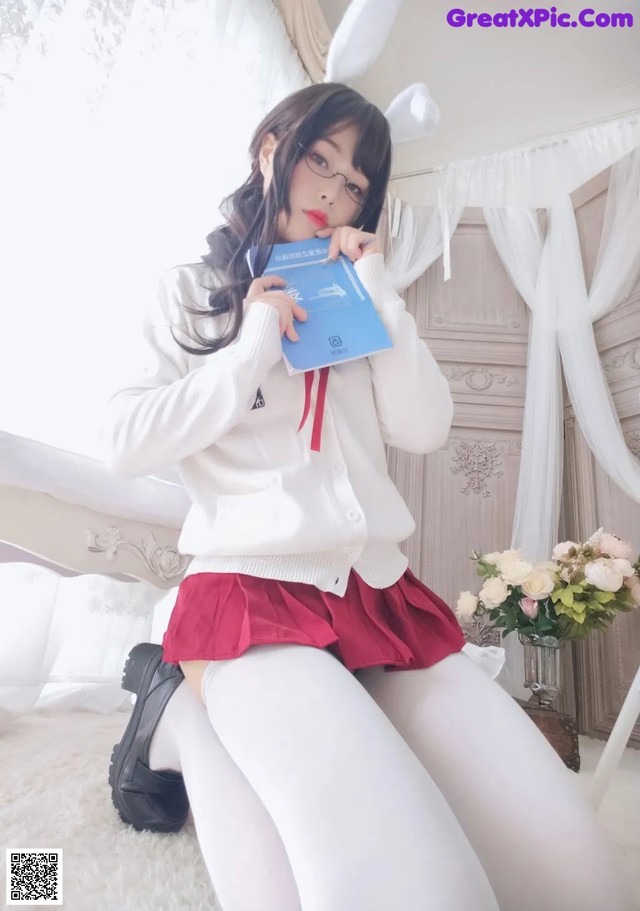 A woman in a white sweater and red skirt holding a book.