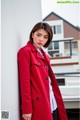 A woman in a red coat leaning against a wall.